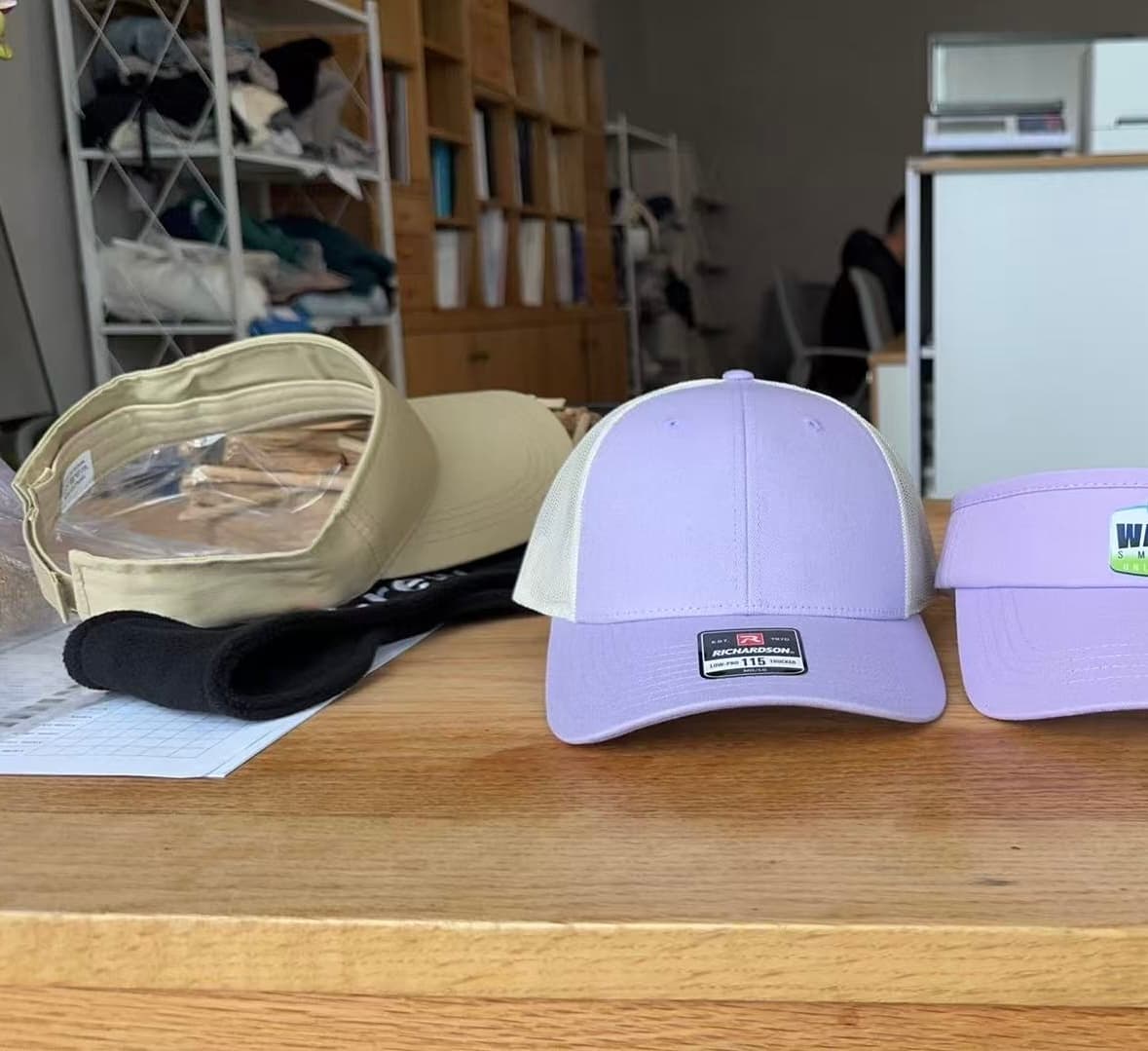 Three custom dad caps — khaki, lavender, and dark green — laid out on a workshop table for comparison