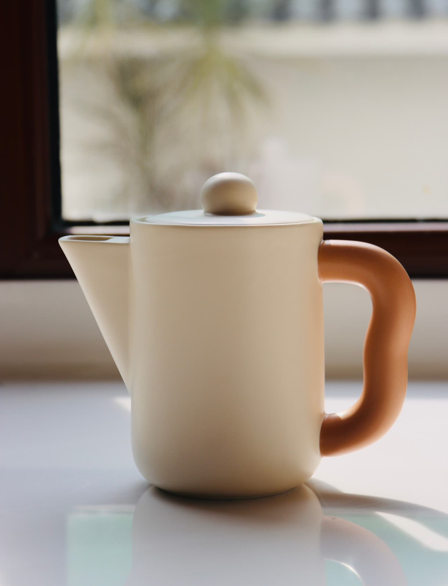 Cream Morandi-style ceramic teapot with peach handle, in window light