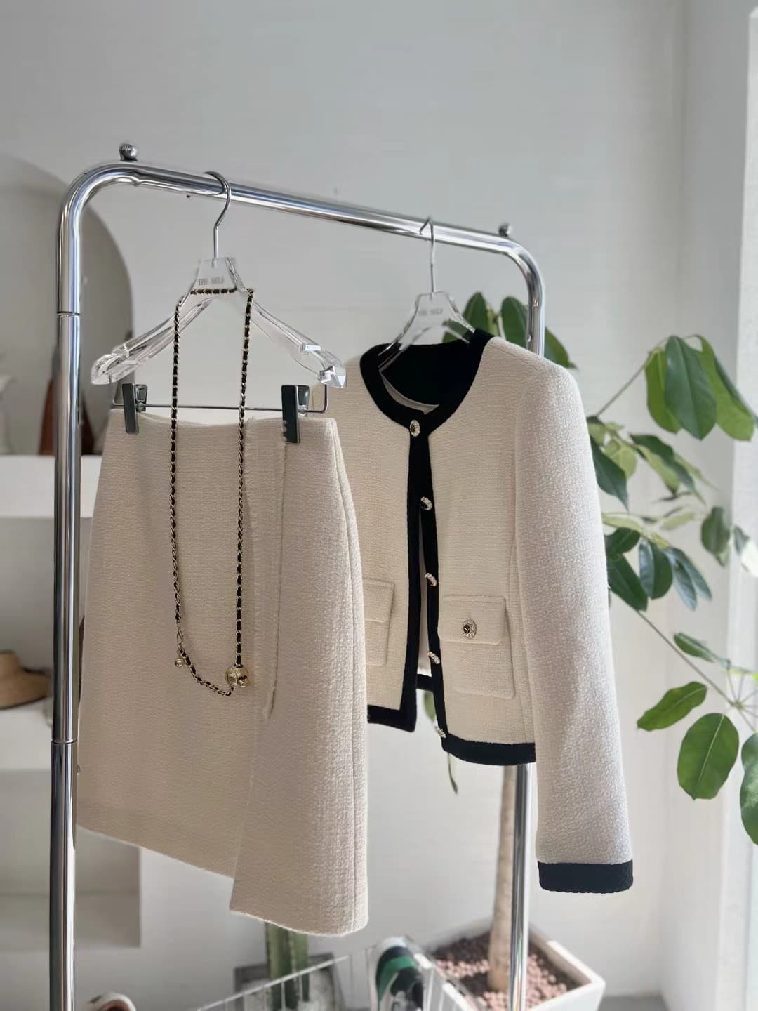 Cream tweed two-piece — collarless jacket with black trim and gold buttons, with matching skirt, on hangers