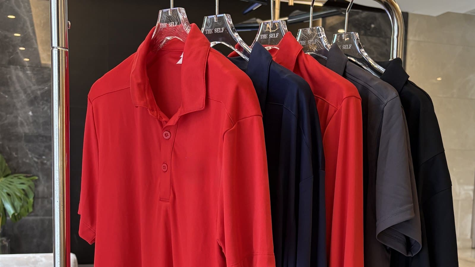 Performance polos in red, navy, grey, and black on a rack, from a multi-brand workwear program