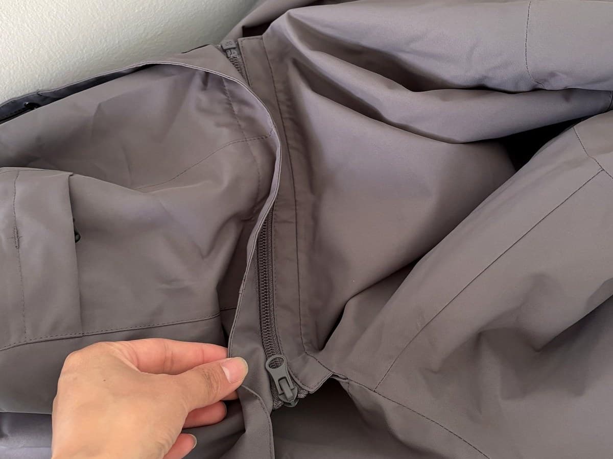 The detachable hood laid out, a hand at the zipper that joins it to the collar